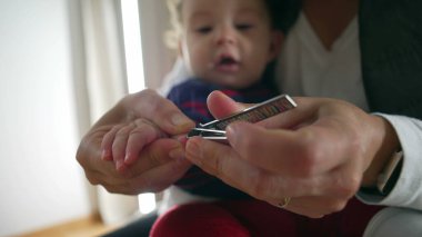 Annenin tırnak makasıyla bebek tırnaklarını kestiği, hassas bakım ve ilgi sağladığı, bebek hijyeni için kişisel bakım yaptığı, odaklanmış ebeveynlik anı..