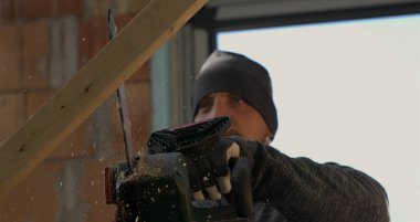 Elektrikli testereyle odun kesen işçiler, 800 fps hızla uçan odun kıymıkları, odaklanmış ifade ve sağlam eller, kapalı alanda ahşap kesme hassasiyeti.