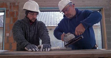 İki inşaat işçisi atölyede açı öğütücü kullanıyor, başlık ve güvenlik teçhizatı takıyor, metal kesim, takım çalışması ve hassasiyetinden kıvılcımlar saçıyor, 800 fp yavaş çekim