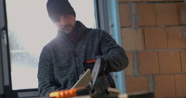 İşçi dikkatli bir şekilde elektrikli testereyi 800 fps 'te yavaş çekimde ahşap tahtadan geçirerek yönlendiriyor, odaklanmış ifade, hassasiyet kesme ve kontrol kapalı alanda.