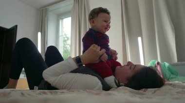 Anne yatakta yatarken bebeği kaldırıyor, oyun oynuyor ve aile evinde kaynaşıyor, birlikte eğleniyor, sevgi ve sevgi dolu bir bağ kuruyor.