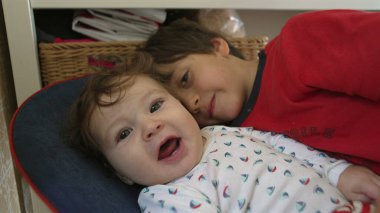 Bebek bir fedaiye uzanıyor, ağabeyinin yüzüne dokunuyor, evde sakin bir aile ortamında nazik bir kardeş etkileşimi.