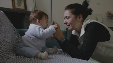 Anne bebekle kanepede iletişim kuruyor, şakacı yüz yüze iletişim kuruyor, erken çocukluk gelişiminde neşe ve bağlılık gösteriyor, ev ortamını büyütüyor.