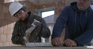 Açı öğütücü metal kesimi sırasında kıvılcımlar çakıyor, koruyucu ekipmanlı işçiler inşaat işinde işbirliği yapıyor, sanayi bölgesi süper yavaş çekim altında.