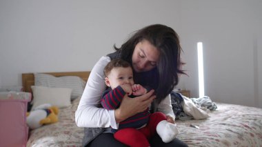 Anne neşeyle bebeği öpüyor, yatakta sevgi dolu ve neşeli anları paylaşıyor, aile evinde samimi ve eğlenceli etkileşimler kuruyor, bebek gülümsüyor ve anneyle bağ kuruyor.