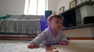 Bebek yerde yatıyor, iki koluyla itiyor, merakla ileri bakıyor, rahat bir yuva ortamında çevreyi keşfediyor, emeklemeyi öğrenmenin ilk aşamaları..