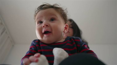 Anne bebeğin başını nazikçe tutuyor, bebek kucağında otururken neşeli bir etkileşim, aile evinde bir bağ kurma anı, ebeveynler ve çocuklar arasında bir bağ..