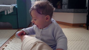 Bebek, anne bacağının üzerinde tuhaf bir ifadeyle dinleniyor, evde aile bağlarını kurma zamanı, bebek ve anne arasında oyuncu ve besleyici bir an, dokunsal bir merakla dünyayı keşfediyor..