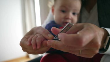 Annenin tırnak makasıyla bebek tırnaklarını kestiği, hassas bakım ve ilgi sağladığı, bebek hijyeni için kişisel bakım yaptığı, odaklanmış ebeveynlik anı..