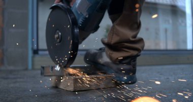 Elektrikli öğütücü metali kesiyor, işçilerin botlarını dengeliyor, kıvılcımlar uçuşuyor, kesinti yapılıyor, endüstriyel ayarlar, yavaş çekim, 800 fp..