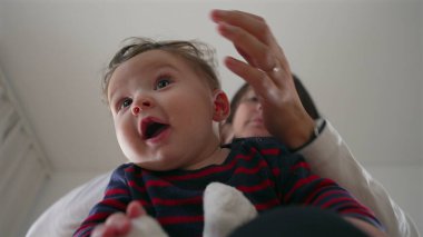 Anne bebeğin başını nazikçe tutuyor, bebek kucağında otururken neşeli bir etkileşim, aile evinde bir bağ kurma anı, ebeveynler ve çocuklar arasında bir bağ..