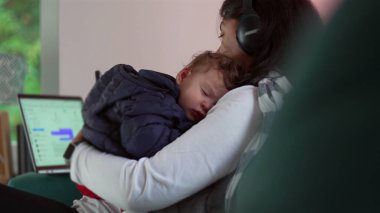 Anne telefonunu kullanırken uyumakta olan bebeği kucağında tutuyor ve dizüstü bilgisayarını kontrol ediyor, iş ve bakıcılık arasında birden fazla iş yapıyor, aile ve kariyer sorumluluklarını birbirine karıştırıyor.