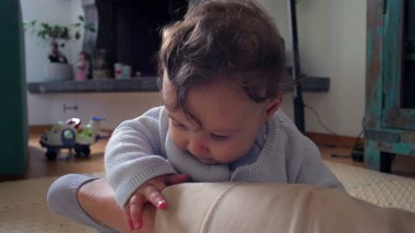 Bebek, anne bacağının üzerinde tuhaf bir ifadeyle dinleniyor, evde aile bağlarını kurma zamanı, bebek ve anne arasında oyuncu ve besleyici bir an, dokunsal bir merakla dünyayı keşfediyor..