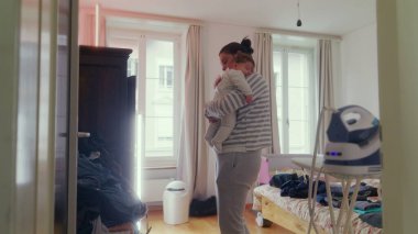 Anne yatak odasında durmuş bebeğe hafifçe dokunuyor. Emziriyor, rahatlatıyor ve büyütüyor. Huzurlu bir yuvada samimi bir bakım yapıyor..