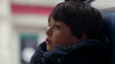 Hareket halindeki bir otobüsün penceresinde oturan genç çocuk, derin düşüncelere dalmış, sessizce geçen manzarayı seyrediyor.