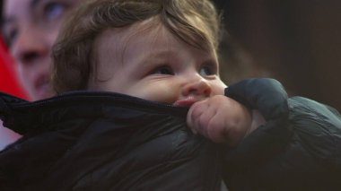 Bebek ceketi, yukarı bakıyor, kışlık palto giyiyor, sıcak aile manzarası, meraklı ve düşünceli ifade, sıcaklık ve koruma, günlük iç mekan sahnesi