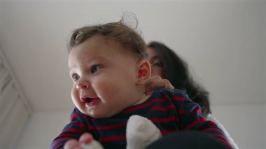 Anne bebeğin başını nazikçe tutuyor, bebek kucağında otururken neşeli bir etkileşim, aile evinde bir bağ kurma anı, ebeveynler ve çocuklar arasında bir bağ..