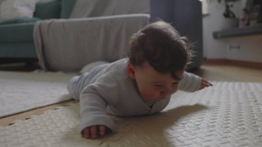 Bebek mindere uzanıyor, başını kaldırıyor ve odaklanmış ifade ile çevreyi keşfediyor, sakin bir ev ortamında erken gelişim ve motor becerilerle meşgul oluyor