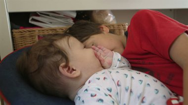 Bebek bir fedaiye uzanıyor, ağabeyinin yüzüne dokunuyor, evde sakin bir aile ortamında nazik bir kardeş etkileşimi.