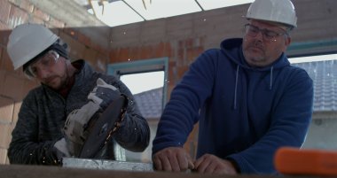 İki adam, metal kesiciyle kesmeye, bitmemiş inşaat sahasında aydınlatma kıvılcımlarına odaklanmış, süper yavaş çekim.