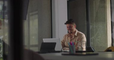 Genç adam laptopta başarıyı ofis işi sırasında neşeli bir tepkiyle kutluyor, modern çalışma alanında gülümseyerek ve tezahürat yaparak.