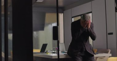 Şirket yöneticisi, sessiz bir ofiste tek başına otururken yüzünü ellerle kapatarak duygulara boğuldu.