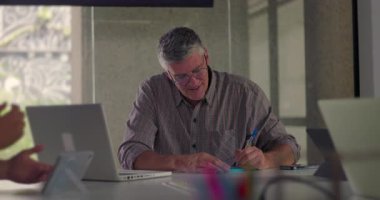 Olgun iş adamı, elinde kalem tutarken ve modern konferans masasında bilgileri incelerken sessiz ofis toplantısı sırasında dizüstü bilgisayarda dikkatle çalışıyor.