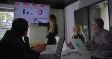 Çeşitli takımlar şirket toplantı odasındaki dijital ekranda görselleri dinlerken ve gözlemlerken genç iş kadını sunumu yönetiyor.