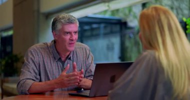 İş adamı, ofis masasında önlerinde dizüstü bilgisayarla kadın meslektaşlarına proje planını anlatıyor.