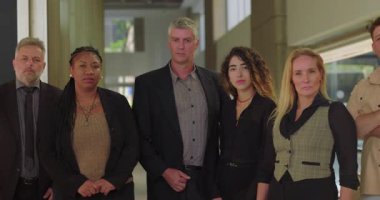 Gülümseyen iş adamları, parlak ofis koridorlarında yakın poz veriyorlar. Çeşitli profesyonel gruplar, pozitif ifade ile günlük iş portresi için birlikte duruyorlar.