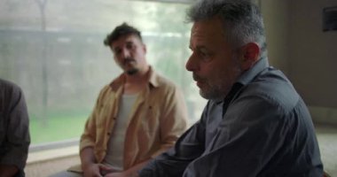 Grup terapisi sırasında ciddi bir şekilde konuşan, akranları olarak duygusal yükü açık bir şekilde ifade eden, destekleyici ortamlarda şefkatle dinleyen bir adam.