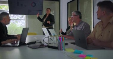 İş kadını, konferans odasında sunum sırasında bağlı ekibe açıklarken ekrandaki veri görselleştirmesine işaret ediyor