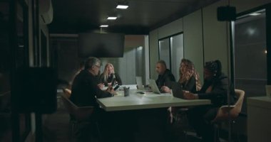 Resmi toplantı odasındaki iş adamları akşam saatlerinde cam ofis içindeki beyaz konferans masasının etrafında dizüstü bilgisayarlar ve tabletler üzerinde çalışıyorlar.