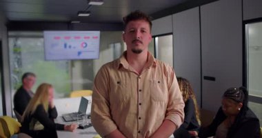 Modern ofiste kendinden emin duran genç işadamı, elleri cebinde, ciddi ifadeler, analitik ekranın yanında çalışan iş arkadaşları