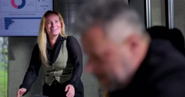 Ofis toplantısı sırasında gülen iş kadını, gelişigüzel ve rahat atmosfer, arka planda grafikler, iş yerinde eğlenen profesyonel kadın.