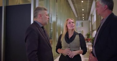 Ofis koridorunda sohbet eden gülümseyen profesyoneller, fikir alışverişi yapan meslektaşlar ve parlak modern işyeri ortamında bağlantı kurmak.