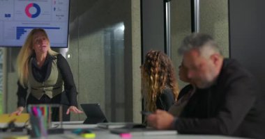 Kadın yönetici, yoğun ofis toplantısı sırasında erkek meslektaşının düşüncelere dalmasına engel oldu. Liderlik hakimiyeti ve işyeri gerginliğinin altını çizdi.
