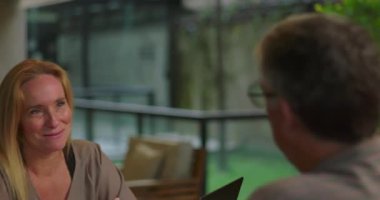 Erkek, modern kapalı çalışma alanındaki masadaki gündelik ofis toplantısı sırasında kadın meslektaşını dikkatle dinliyor.