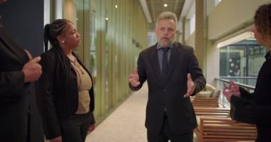 Ofis koridorundaki küçük bir grup meslektaşla konuşan yönetici, profesyonel çevrede kendine güvenen vücut diliyle iş yerinde tartışmalara öncülük ediyor