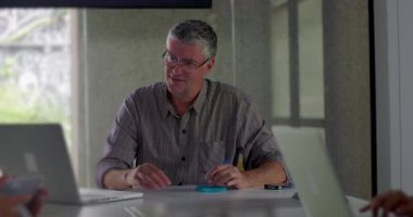 Odaklanmış işadamı, ofis toplantısı sırasında laptoplar ve takım arkadaşlarıyla birlikte toplantı masasında otururken el yazısıyla notlar alır.