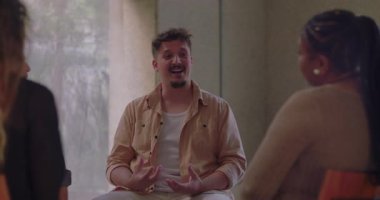 Terapi grubunda yürekten konuşan bir adam, özenli ve destekleyici katılımcılarla çevriliyken kişisel hikayelerini paylaşmak için anlamlı jestler kullanır.