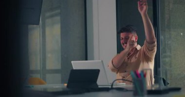 Genç adam keyifli bir kutlama için kollarını kaldırıyor. Tek kişilik ofis çalışması sırasında dizüstü bilgisayarda başarılı bir andan sonra.