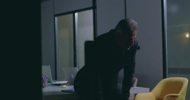 Şirket yöneticisi, yoğun bir iş toplantısından sonra karanlık ofiste konferans masasına yaslanıyor.