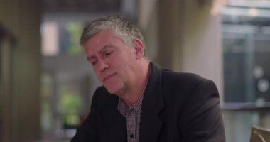 Orta yaşlı bir adam ofis odasında gözleri kapalı ve kederli bir ifadeyle oturuyor, sessiz çalışma alanında pişmanlık ya da duygusal rahatsızlığı iletiyor.