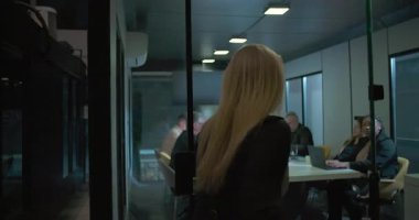 Gece modern ofisteki çeşitli ekiplerle iş toplantılarında iş arkadaşlarına hitap etmek için yönetim kuruluna giren bir kadın yönetici.