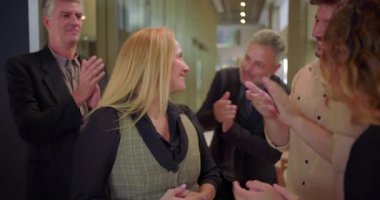 Ofis koridorundaki çeşitli iş arkadaşlarından alkış alan gülümseyen kadın, başarıyı kutlayan ve iş yerinde takdir gösteren bir grup profesyonel.