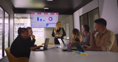 Takım dinlerken ve dijital grafikler modern ofis ortamında anahtar ölçülerini gösterirken, sarışın profesyonel gülümseme