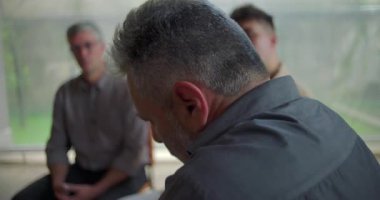 Terapi seansı sırasında konuşmaya hazırlanan sıkıntılı adama yakın durun. Destek grubu duygusal güven ve iyileşme ortamını dinlerken yoğun bir yansıma anı.