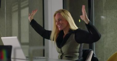 Modern ofis ortamındaki iş toplantısı sırasında dizüstü bilgisayara bakarken heyecanlı kadın yöneticiler tezahürat yapıyor ve başarıyı kutluyor.