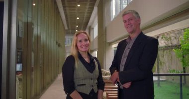 Profesyonel erkek ve kadın ofis koridorunda güven içinde poz veriyorlar. İş ortakları parlak şirket koridorunda birlikte duruyorlar.